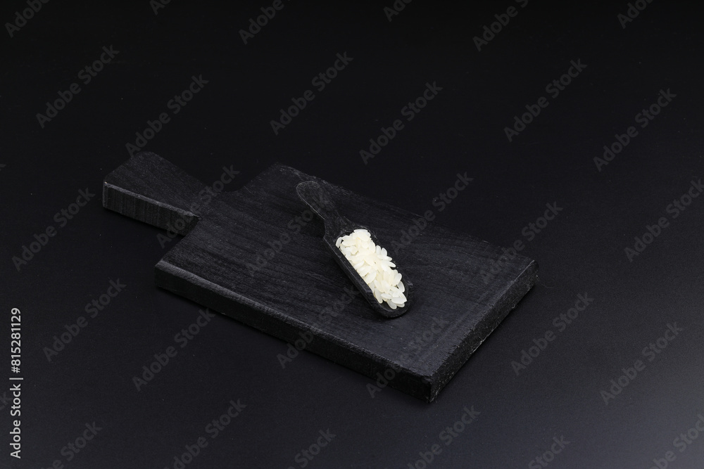 Raw white rice on black background. Long uncooked rice in wooden plate. Natural organic food. Traditional Asian cereal culture. Raw white rice on black background. Long uncooked rice in wooden plate. Natural organic food. Traditional Asian cereal culture.
