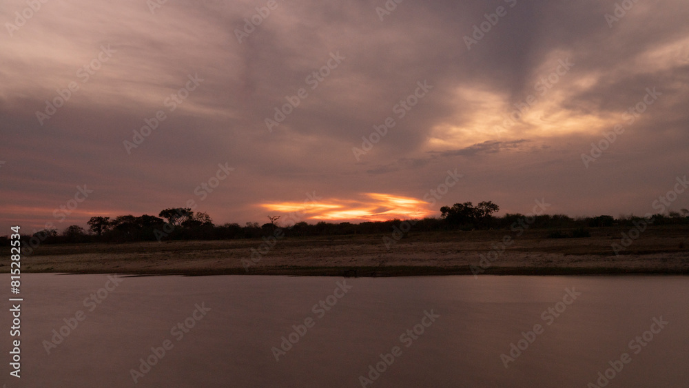 Long exposure shot of Corriente river in Esquina, Corrientes, Argentina, at sunset. Beautiful blurred water effect, dramatic clouds and hiding sun at nightfall.