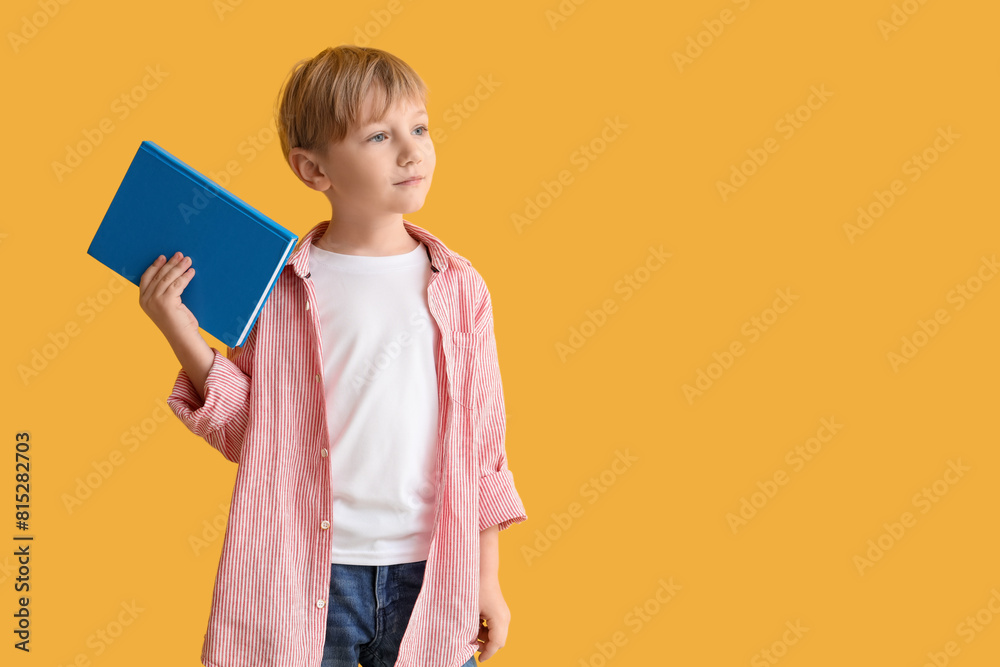 Cute little boy holding book against yellow wall Cute little boy holding book against yellow wall
