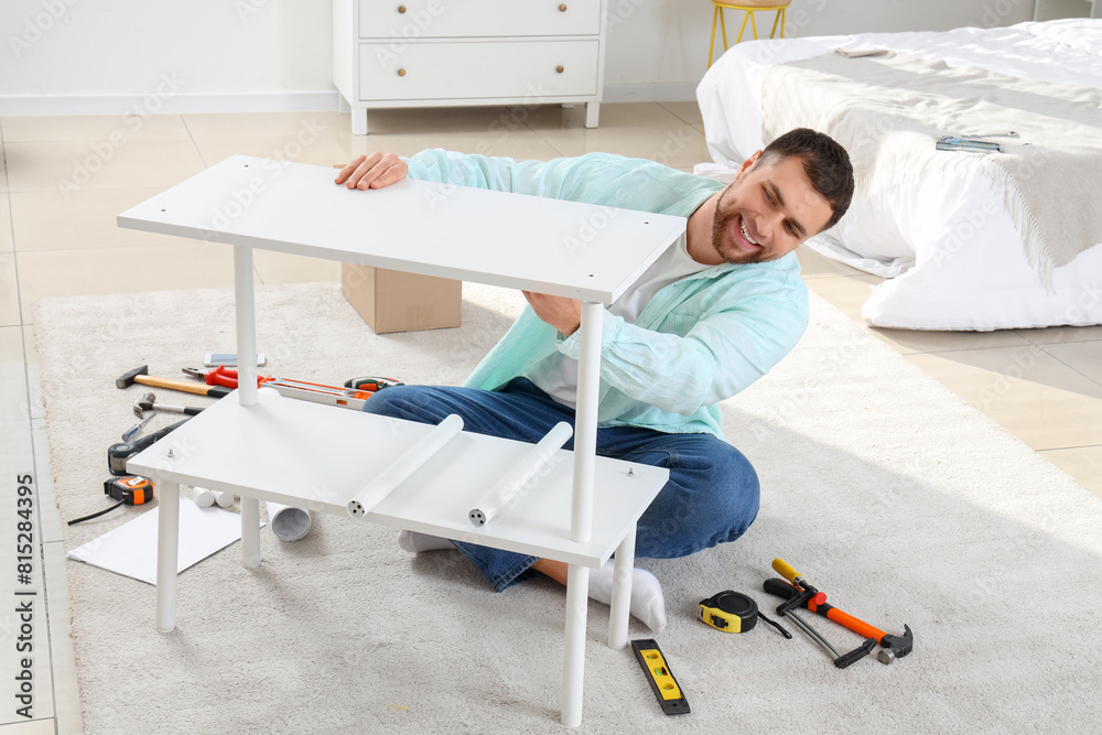 Fototapeta premium Young man assembling white shelf unit in bedroom