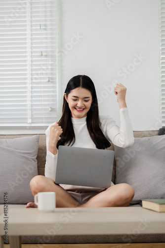 A woman is sitting on a couch with a laptop in front of her. She is smiling and she is happy