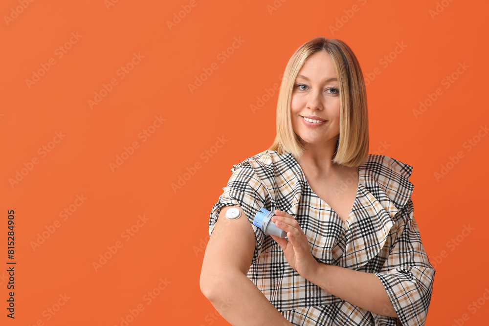 Woman with glucose sensor for measuring blood sugar level and applicator on orange background. Diabetes concept Woman with glucose sensor for measuring blood sugar level and applicator on orange background. Diabetes concept