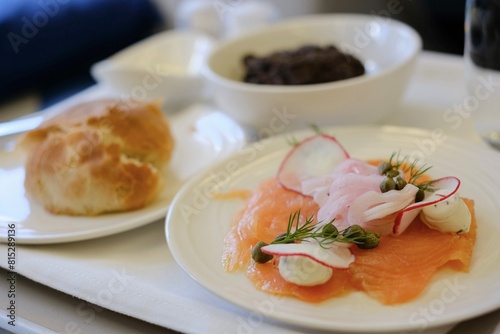 An entree of smoked salmon with herbed cream cheese, red radish, capers, pickled onion, fresh bread rolls, a pat of butter and cookies and cream cheesecake on a business class flight from Sydney to KL