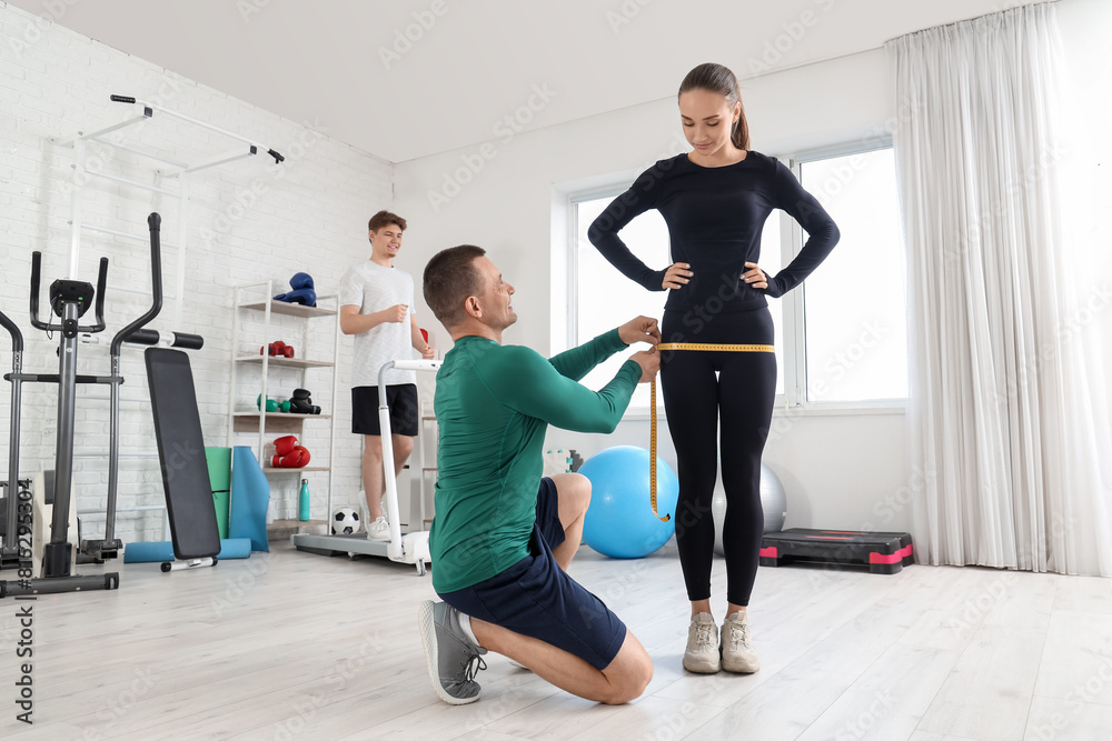 Obraz premium Male trainer measuring young woman's hips in gym