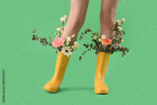 Foto Woman with flowers in gumboots on green background, closeup
