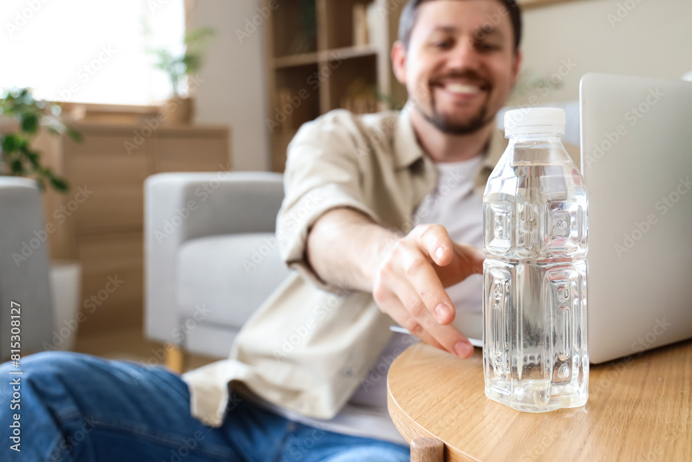Young man taking bottle of water from table at home, closeup Young man taking bottle of water from table at home, closeup