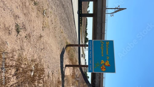 Welcome to California sign. Vertical static shot of state border sign along interstate highway with traffic in desert. Entering Pacific Time Zone. photo