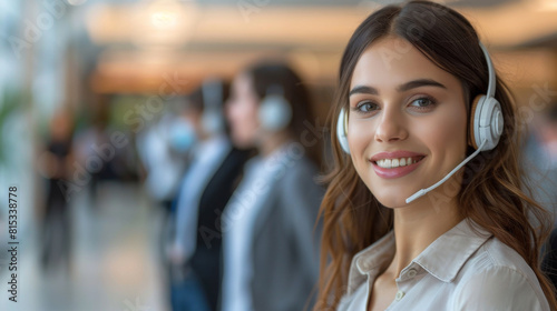 Young female customer service representative wearing a headset and smiling in a busy office environment.