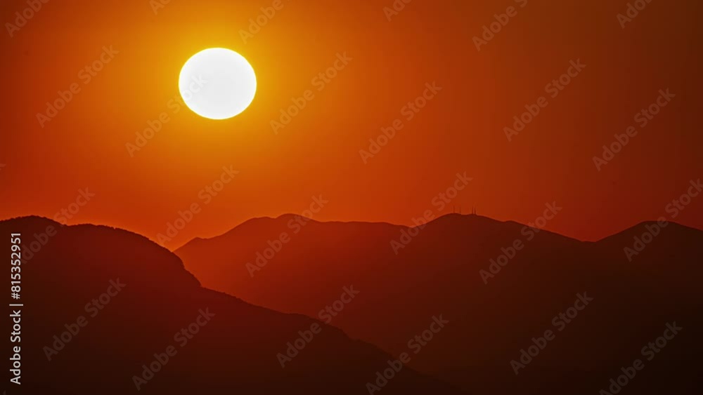 Glowing golden sun setting behind the silhouette of a mountainous landscape - time lapse