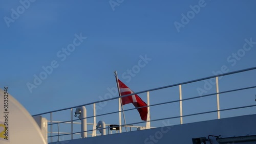 Danish national flag fluttering hung on a metal mast on the upper deck of a ferry, beautiful sunny evening photo