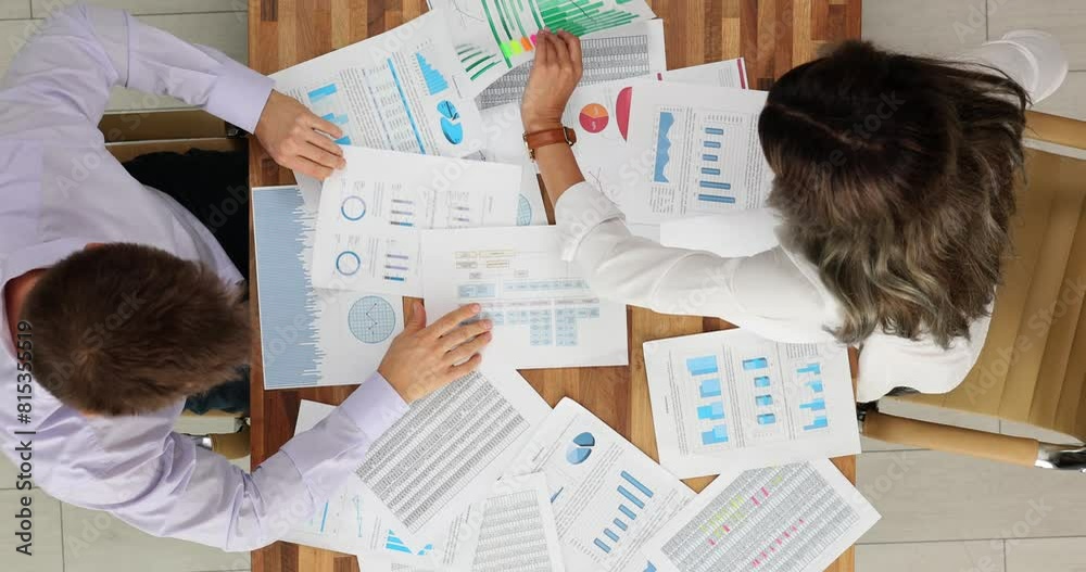 Two business professionals nervously analyzing business documents, top view