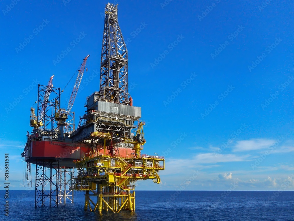Drilling rig offshore oil field showing derrick, drill floor, crane, well slot platform, leg with clear blue sky background. High resolution industry image