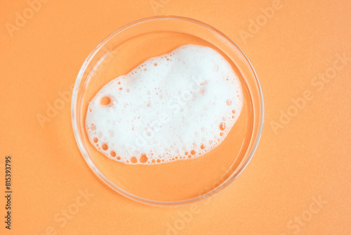 Smear of facial cleansing foam in petri dish on orange background close-up.