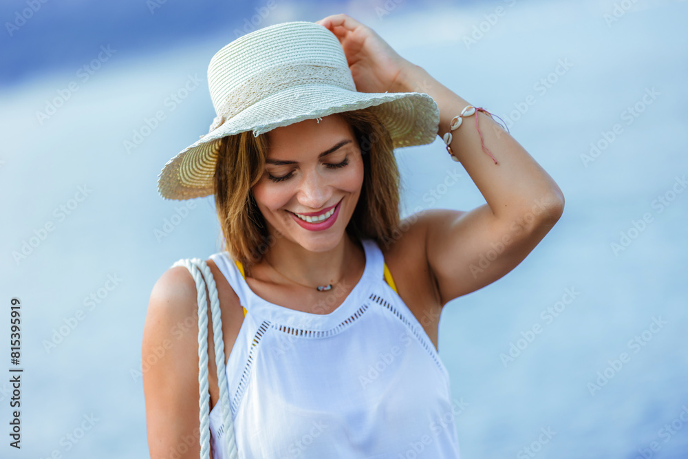 Happy young beautiful woman walking alone on the beach with beach bag and hat.