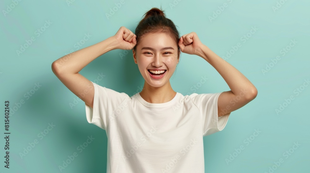 Joyful Asian woman playfully pulls her hair up, laughing against a light turquoise background Joyful Asian woman playfully pulls her hair up, laughing against a light turquoise background