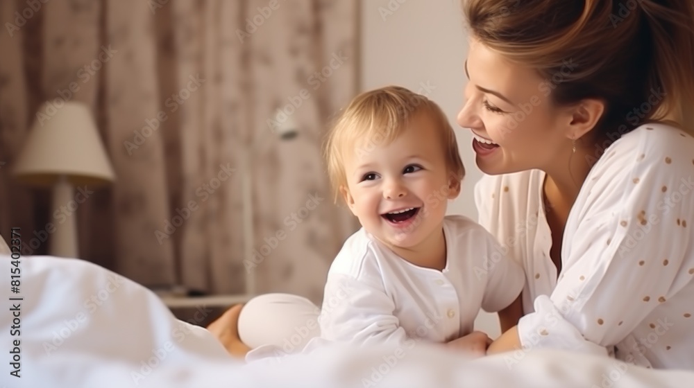 Loving mother playing with her toddler son in bed, smiling joyfully, cozy atmosphere