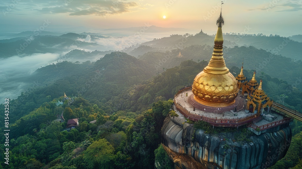 Aerial view of the Kyaiktiyo Pagoda (Golden Rock) in Myanmar, featuring the golden boulder balancing on the edge of a cliff with surrounding forested hills.     