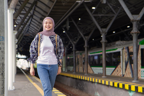 happy asian muslim woman wearing casual outfit walking on train station platform. traveling concept © Ibenk.88