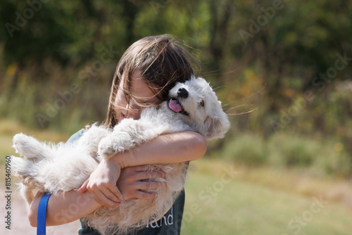 Joyful girl holding a playful white puppy outdoors on a sunny day