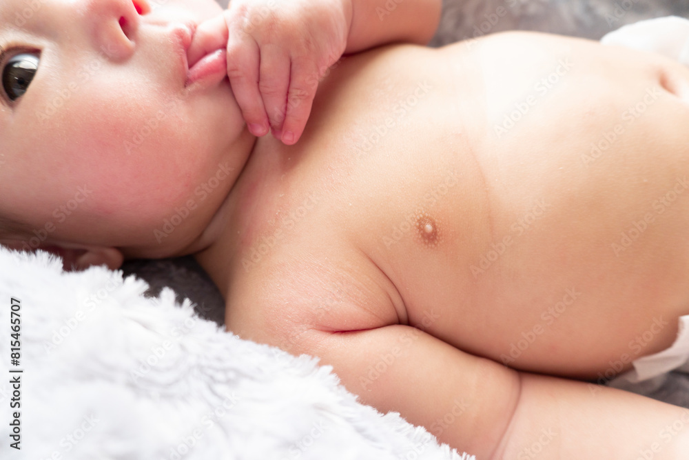 Naked Japanese baby boy with red dry skin lies down on a comfortable gray bed and sucks his thumb Naked Japanese baby boy with red dry skin lies down on a comfortable gray bed and sucks his thumb