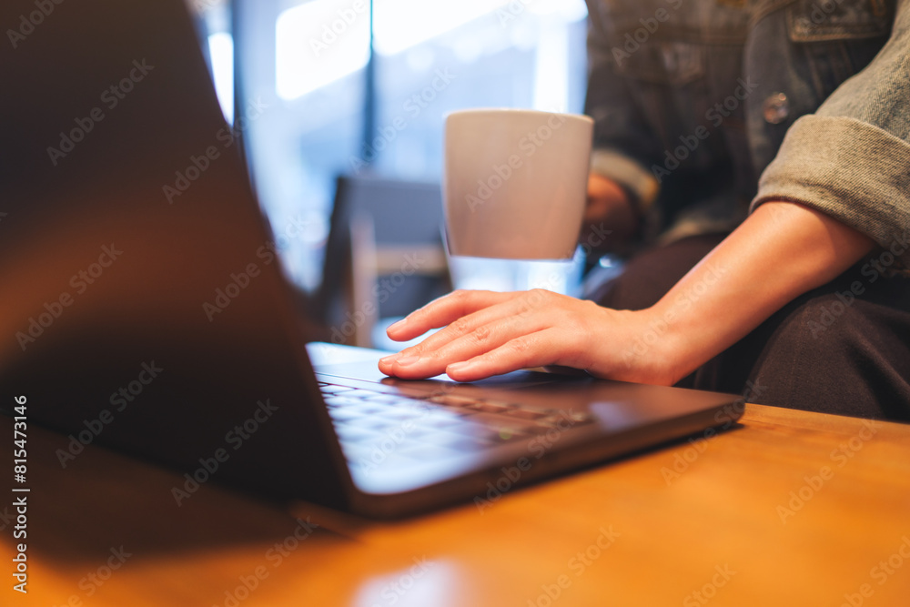 Closeup image of a woman working and touching on laptop computer touchpad while drinking coffee in cafe Closeup image of a woman working and touching on laptop computer touchpad while drinking coffee in cafe