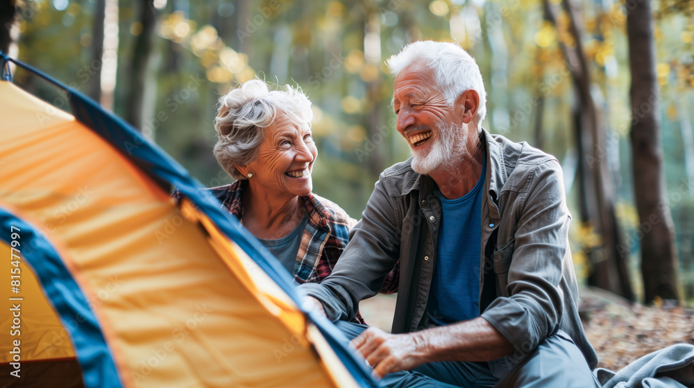 An older couple relaxes as they sit in front of a tent pitched in the woods, enjoying nature and each others company An older couple relaxes as they sit in front of a tent pitched in the woods, enjoying nature and each others company