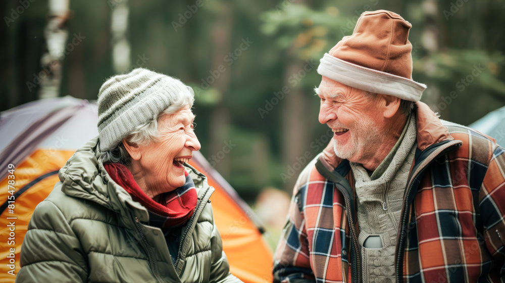An elderly couple is joyfully laughing together in front of a camping tent in the great outdoors