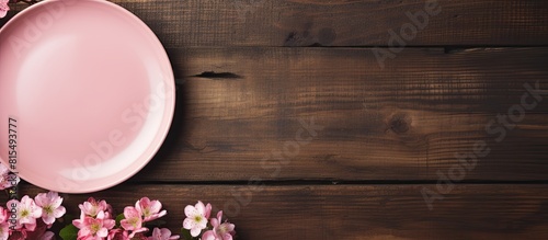 A pink plate with flowers is placed on a wooden table The background is colorful and empty The image has ample empty space