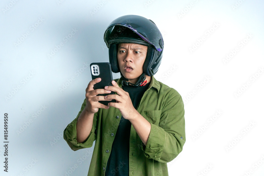 Adult Asian man confusing when looking to his handphone while wearing motorcycle helmet. Man looking to his phone with shocked expression Adult Asian man confusing when looking to his handphone while wearing motorcycle helmet. Man looking to his phone with shocked expression