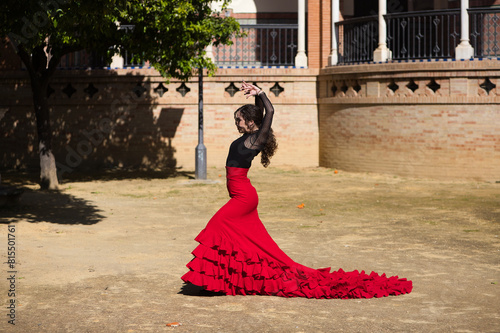 Beautiful woman dancing flamenco in Seville, Spain. She is wearing a red and black gypsy dress and dancing flamenco with a lot of art. In the background a monument with arches and columns.