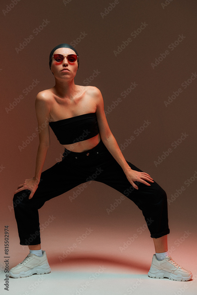 Fashion portrait. A girl in a swimming cap, black top, pants, white sweatshirts and sunglasses poses in the studio. Fashion portrait. A girl in a swimming cap, black top, pants, white sweatshirts and sunglasses poses in the studio.