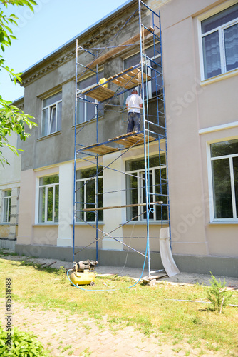 A builder repairs the facade of a house and applies new plaster before painting the exterior walls.