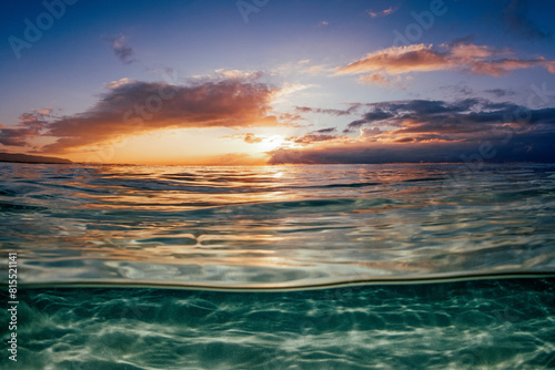 Above and below capture of shallow clear ocean water filled with vibrant sunrise reflections above