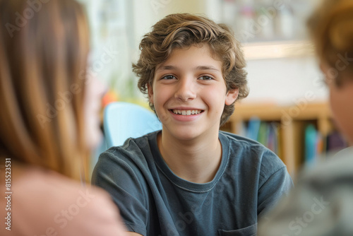 Smiling teenage boy talking with mental health professional while sitting on chair in school office