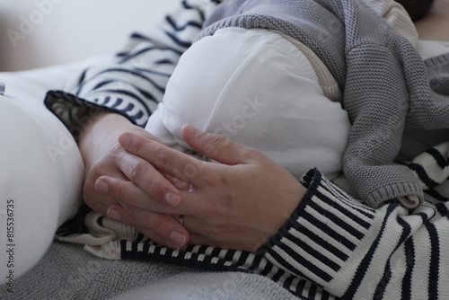 A mother gently holds her newborn baby, who is wrapped in a cozy gray sweater and resting peacefully. The mother's hands are lovingly placed on the baby, creating a scene of tenderness and protection.