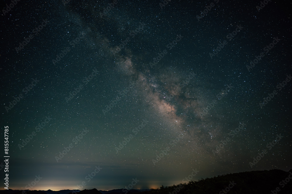 Fototapeta premium 流れ星と共に輝く天の川、森のシルエットが浮かぶ夜空