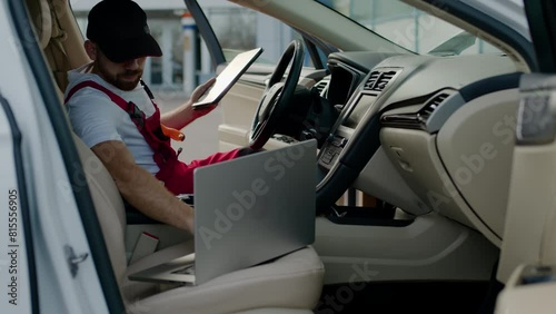 Automotive engineer conducts diagnostic tests on car malfunction using computer sitting inside automobile. Master engineer sitting inside car analyzes car's issues auto service repair shop.