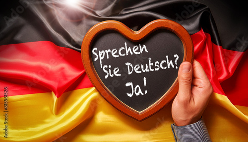Close-up of a hand holding a heart-shaped blackboard with wooden frame and question, Do You Speak German? and Yes! (Sprechen Sie Deutsch? and Ja!). Against a German flag. Generative Ai. photo