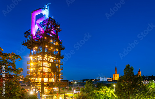 The historic blast furnace in Neunkirchen (Saarland, Germany) is a public sight and attraction. Industrial heritage at blue hour with lights and city skyline.