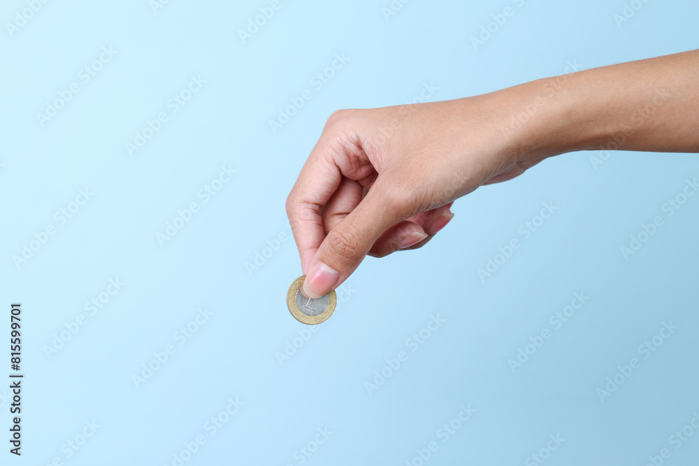 Woman hand holding a coin isolated on blue background Woman hand holding a coin isolated on blue background