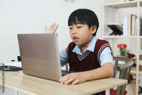 Little boy waving hand to laptop doing online class at home