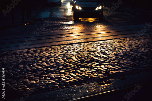 Car lights with highlights on a cobbled road at night