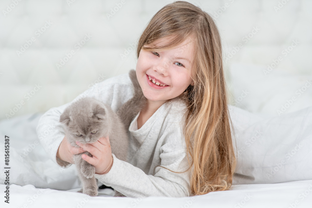 Smiling little girl plays with tiny kitten on the bed at home Smiling little girl plays with tiny kitten on the bed at home
