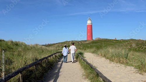 A diverse couple of men and women walking on a path to the lighthouse of Texel surrounded with sand dunes on a beautiful summer day in the Netherlands photo