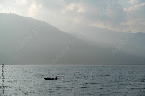 Small boat sailing in the middle of a vast lake surrounded by majestic mountains. © Wirestock