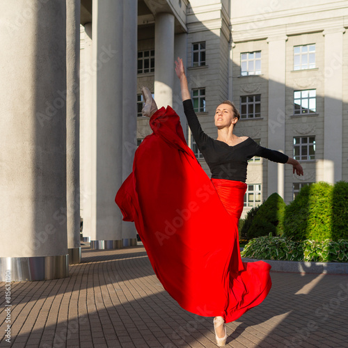 Dancing Flexible Winsome Professional Caucasian Ballet Dancer in Red Skirt in Leg Stretching Dance Pose With Lifted Hands Against Pillars
