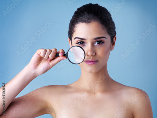 Skincare, portrait and girl with magnifying glass in studio for wellness, treatment and results inspection on blue background. Skin, magnifier or gen z model with face search for dermatology benefit