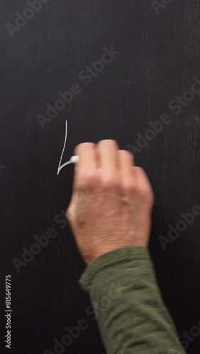 Hand writes the number 5 with white chalk on a black board. Vertical video