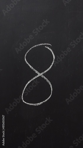 Hand writes the number 8 with white chalk on a black board. Vertical video