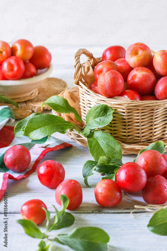 Red fresh ripe plums with water drops in wicker container on white wooden table, organic plums served for eating, healthy food and fruit concept Red fresh ripe plums with water drops in wicker container on white wooden table, organic plums served for eating, healthy food and fruit concept